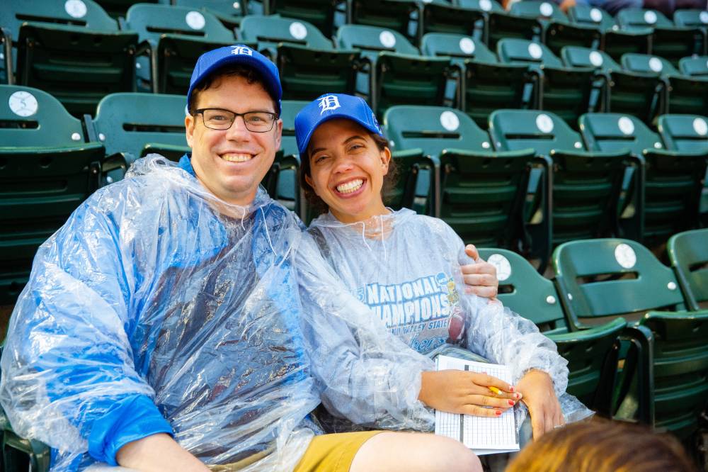 A nice adult couple in ponchos and gvsu night tigers hats sitting in their seats posing together for the photo